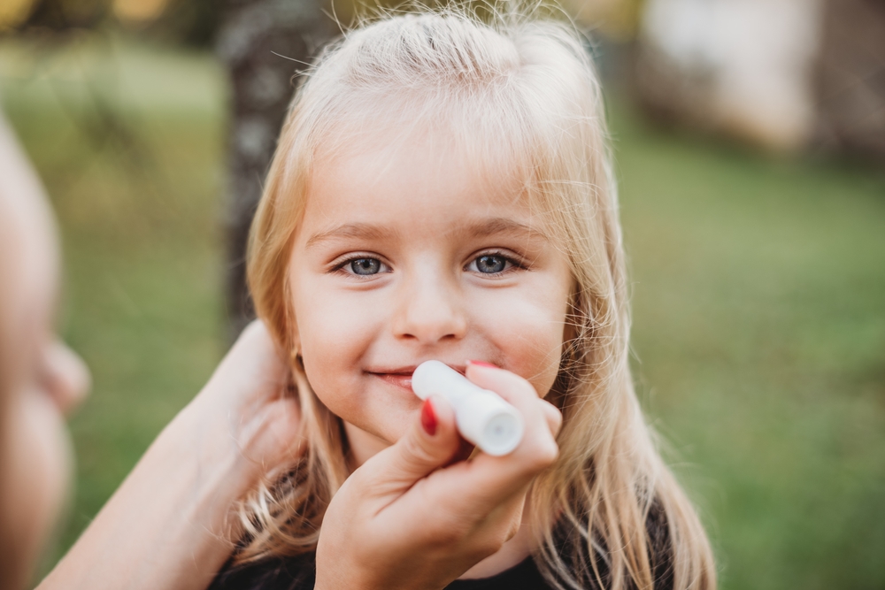 A parent applying baby skin balm to soothe dry cheeks on an infant